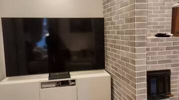 En moderne stue med et stort fladskærms-tv monteret på et hvidt skab, en pejs med murstensmønster og en trægulv.