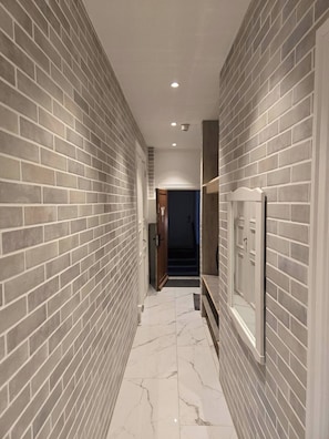 A hallway with brick walls and a marble floor, leading to a dark room.