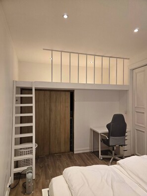 Un dormitorio con cama alta, un escritorio y una silla.