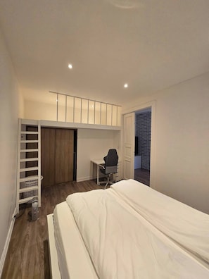 Ein Schlafzimmer mit Bett, Schreibtisch, Stuhl, Kleiderschrank und einem kleinen Balkon.