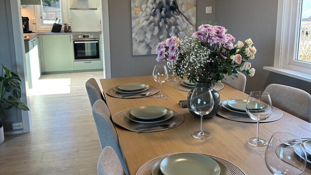 A dining area with a wooden table set for four, a vase of flowers, and a painting on the wall. - Delightful 2-bedroom apartment in charming Lillehammer (Innlandet)