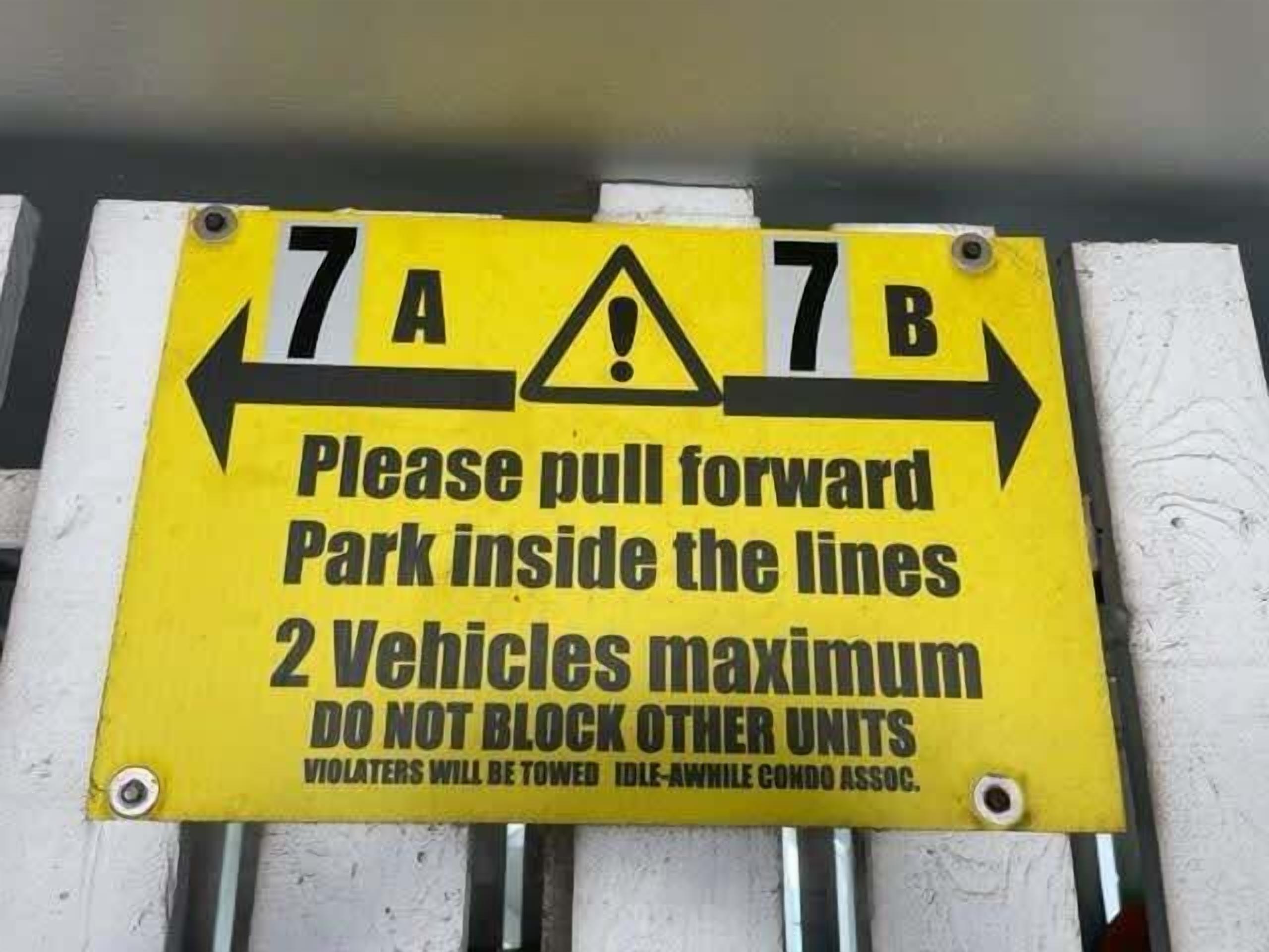 A yellow parking sign with instructions to pull forward and park within lines, a maximum of two vehicles, and a warning that violators will be towed.
