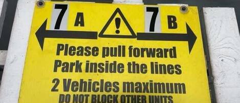 A yellow parking sign with instructions to pull forward and park within lines, a maximum of two vehicles, and a warning that violators will be towed.