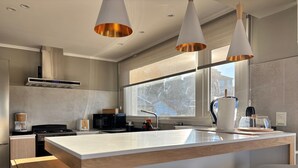 Una cocina moderna con una isla grande, luces colgantes y vistas al exterior a través de un amplio ventanal.