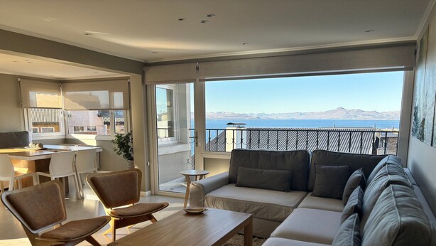 Una sala de estar moderna con sofá, sillas, una mesa de centro y vista al mar.