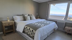 Un dormitorio con una cama grande, una mesita de noche, un radiador y vistas al exterior.