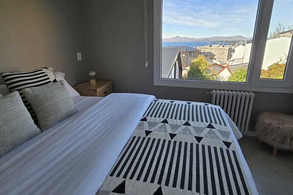 A bedroom with a large bed, a view of the city, and a window with a view of mountains.