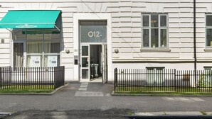 Ein Gebäude mit einer grünen Markise, auf der 'WAX AND BEAUTY LAB' steht, und einer Tür mit der Aufschrift 'O12'.