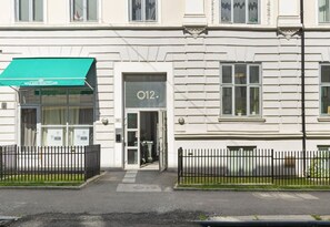 En byggnad med ett grönt solskyddsmärke med texten ”WAX AND BEAUTY LAB” och en dörr märkt med ”O12”.