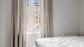 A bedroom with a bed, a window with curtains, and a view of buildings outside.