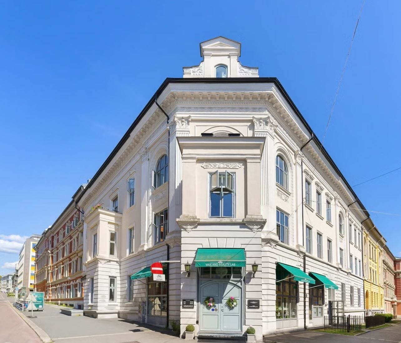 Ein historisches Gebäude mit klassischer Architektur, das einen markanten Eingangsbereich mit einer grünen Markise und einer Gedenktafel aufweist.
