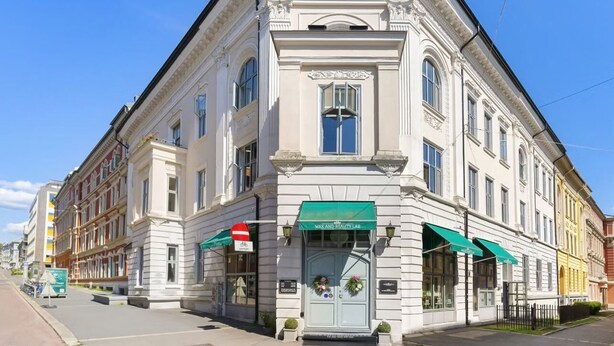 Ein historisches Gebäude mit klassischer Architektur, das einen markanten Eingangsbereich mit einer grünen Markise und einer Gedenktafel aufweist.