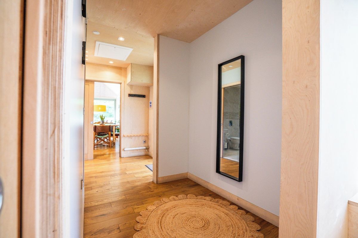 A hallway with wooden flooring, a round woven rug, and a framed mirror on the wall.
