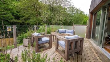 Una terrazza esterna con tavolo e sedie in legno, immersa nel verde e delimitata da una recinzione in legno.