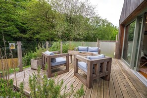 An outdoor deck with a wooden table and chairs, surrounded by greenery and a wooden fence.