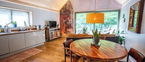 A modern kitchen with a dining area, wooden flooring, and large windows.