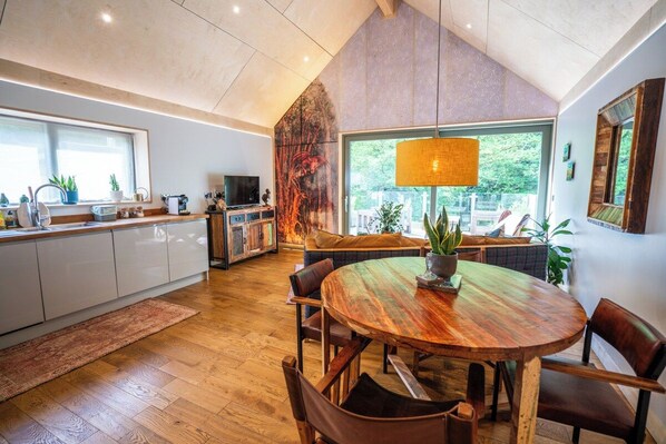 A modern kitchen with a dining area, wooden flooring, and large windows.