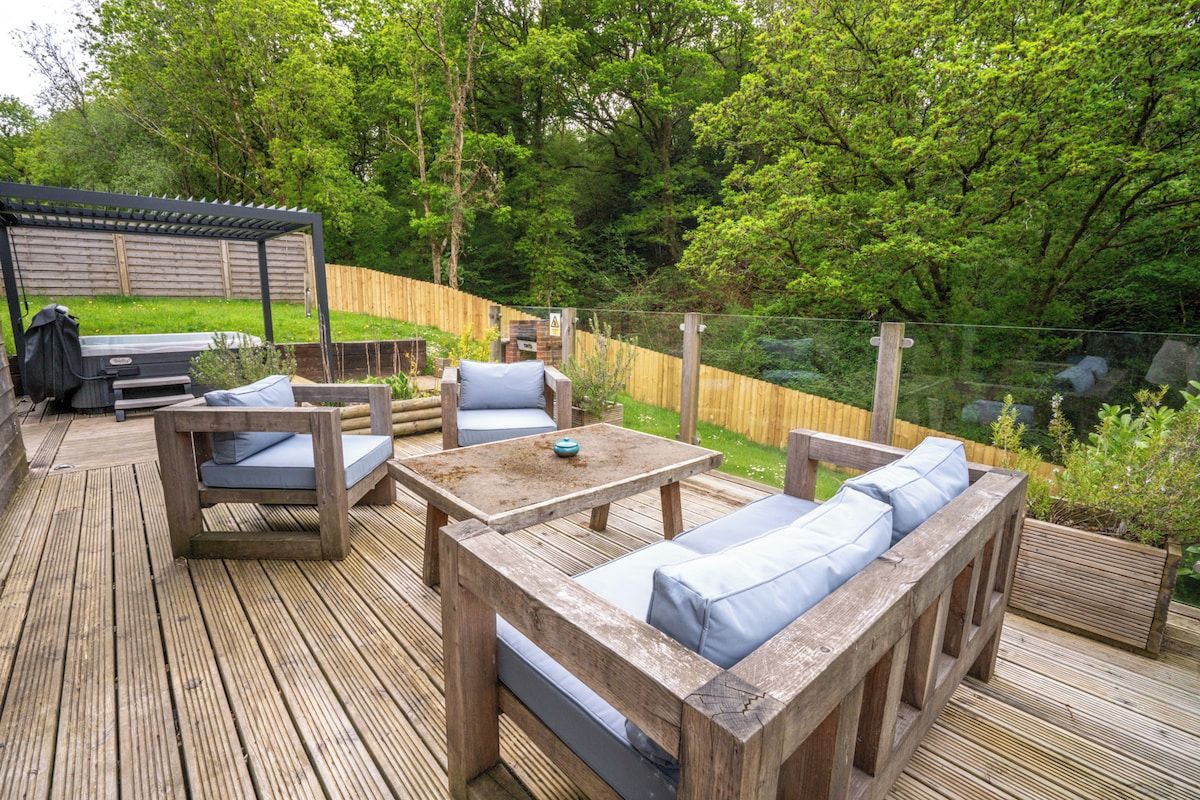 A wooden deck with outdoor furniture, including a sofa and a table, surrounded by a wooden fence and greenery.