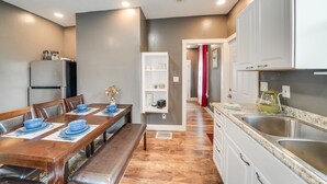Una cocina moderna con horno empotrado, un comedor con mesa de madera y cuencos azules, y un pasillo con cortina roja.