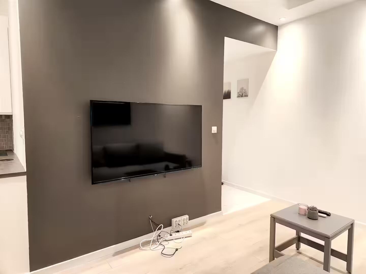 Et moderne værelse med et fladskærms-TV monteret på en mørk væg, et lille bord med et lys og en børste, samt et lyst gulv.