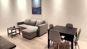 A modern living room with a grey sectional sofa, a small coffee table, a dining table with four chairs, and a large abstract painting on the wall. - P1-Central-Cosy flat Suit All Globetrotters-2rooms (Oslo)