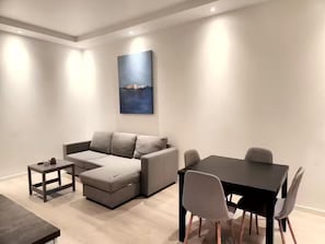 En moderne stue med en grå hjørnesofa, et lille sofabord, et spisebord med fire stole og et stort abstrakt billede på væggen.