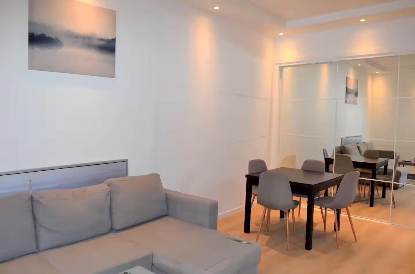 A modern room with a grey sofa, a dining table with chairs, and a large glass partition.