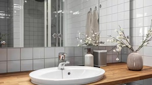 Un bagno moderno con un lavandino bianco, un piano d'appoggio in legno e uno specchio che riflette l'area doccia.