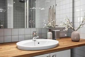 Ett modernt badrum med en vit tvättställ, en bänkskiva i trä och en spegel som reflekterar duschhörnan.