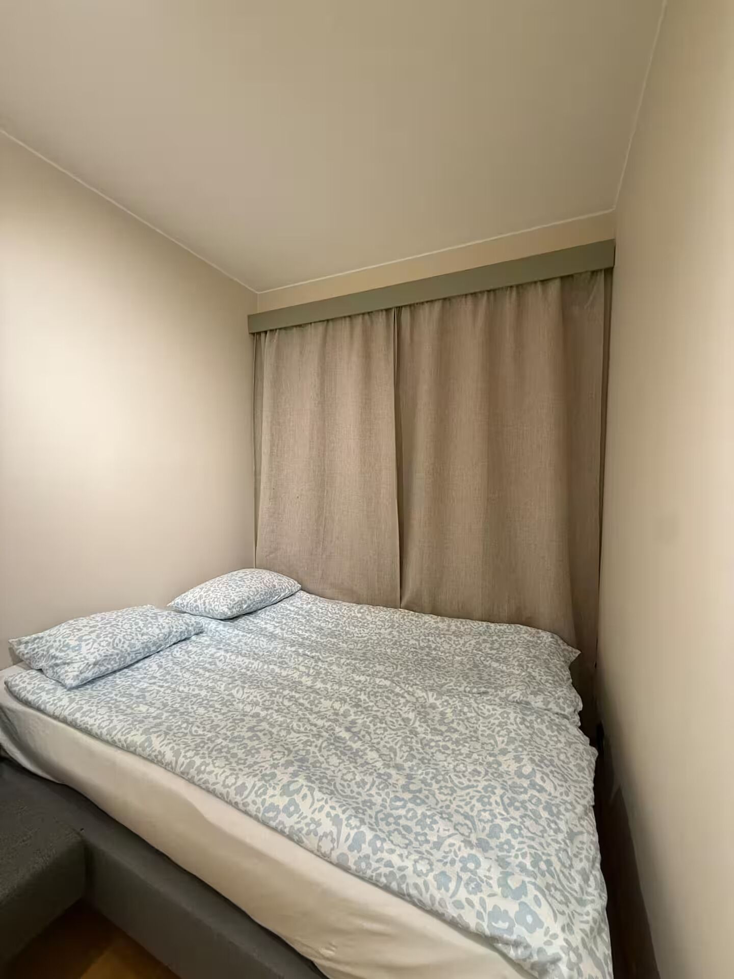 A bedroom with a bed, a window with curtains, and a small bedside table.