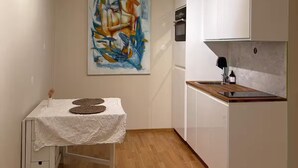 Una cucina compatta con mobili bianchi, un piano di lavoro in legno e un piccolo tavolo da pranzo con tovaglia bianca.