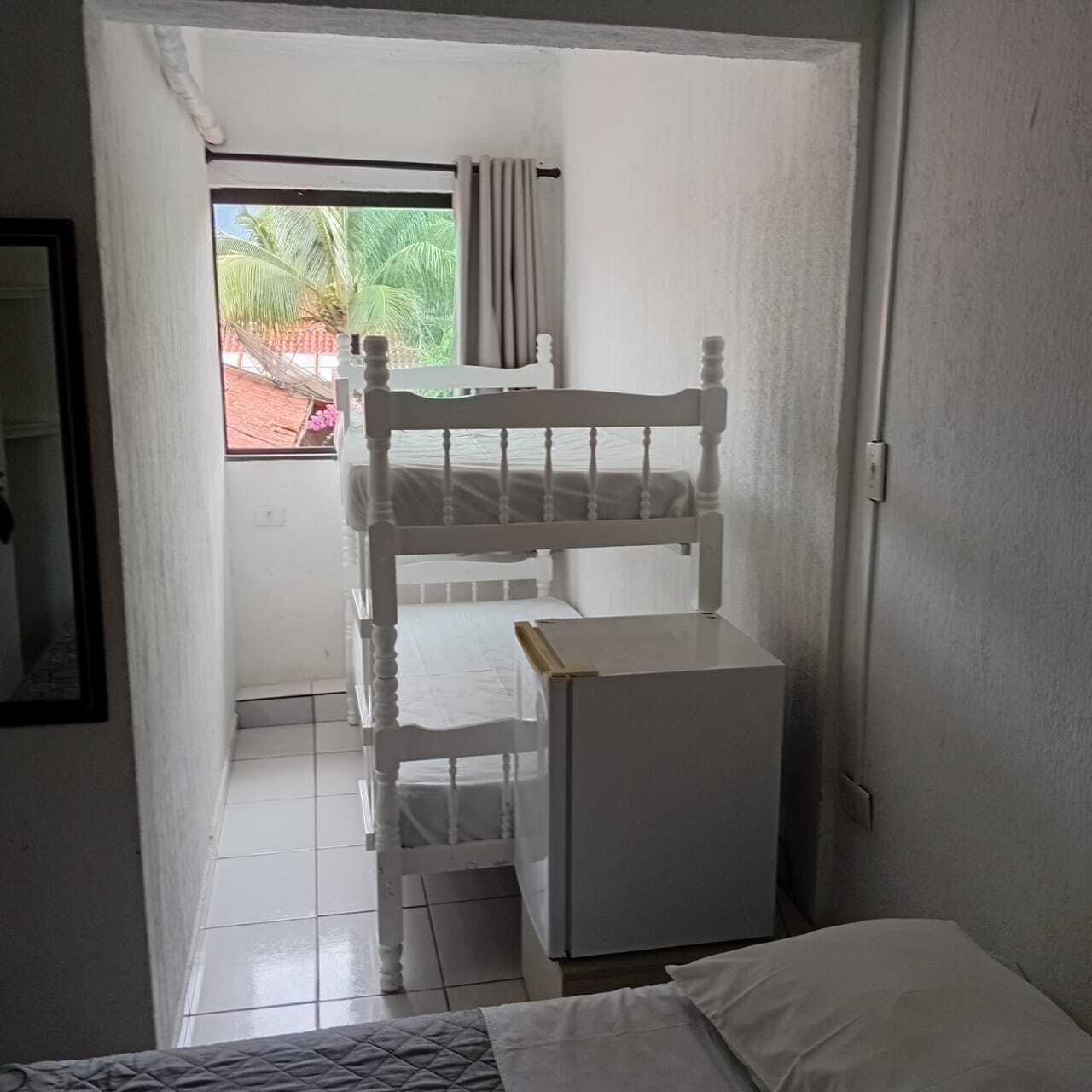 A small, narrow room with a bunk bed, a small table, and a window with curtains.