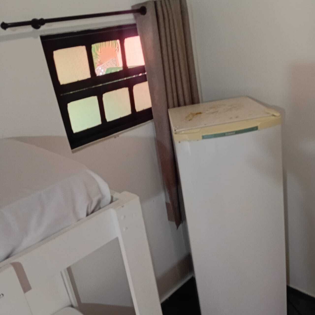 A small, single-bed room with a window and a white wardrobe.