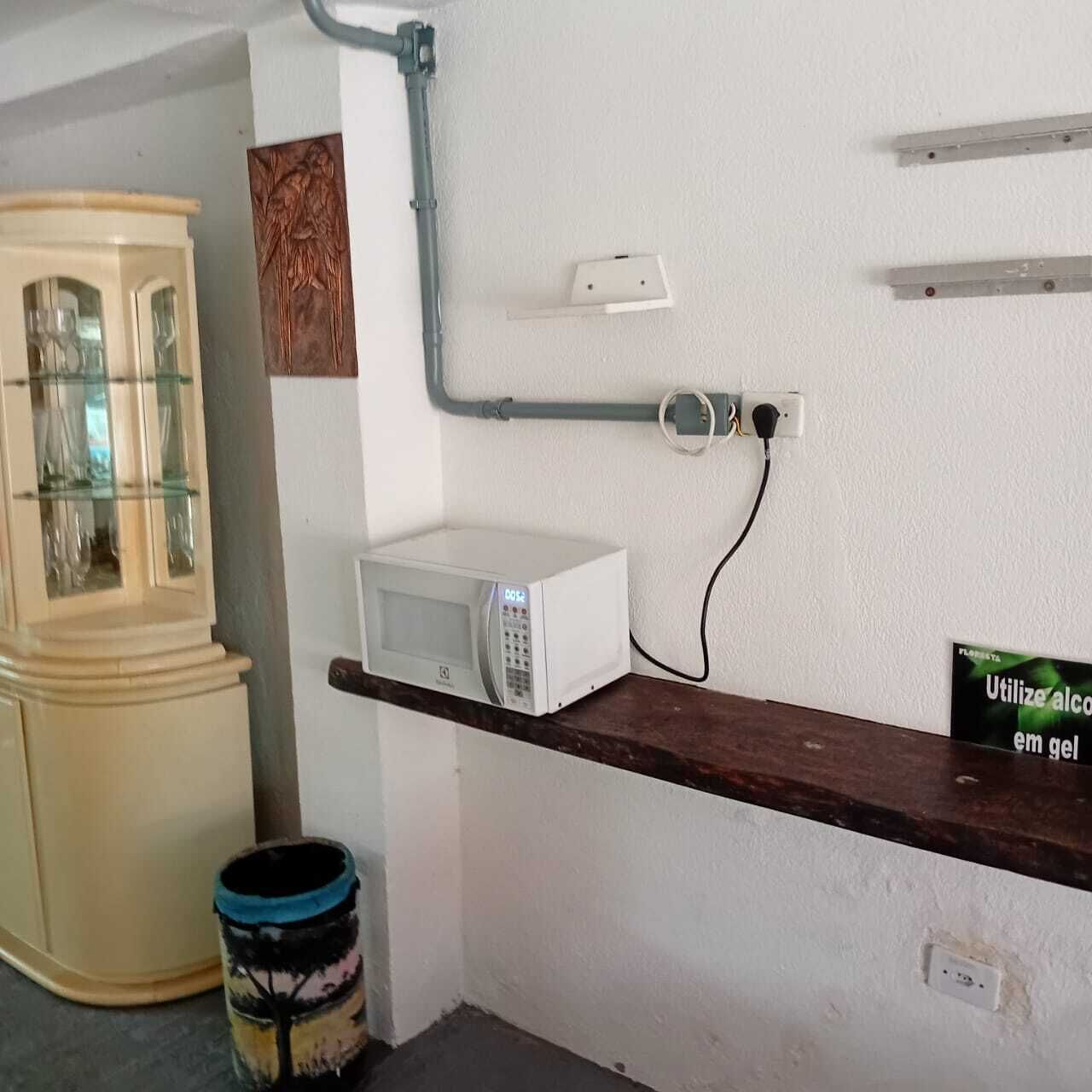 Une cuisine avec un four à micro-ondes posé sur une étagère en bois, un meuble avec des portes en verre et une poubelle.