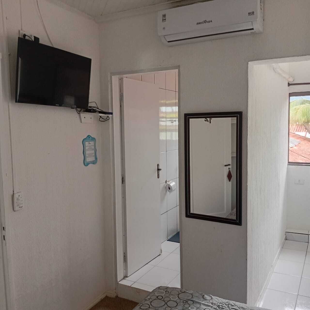 A room with a bed, a TV mounted on the wall, a door leading to another room, and an air conditioning unit.