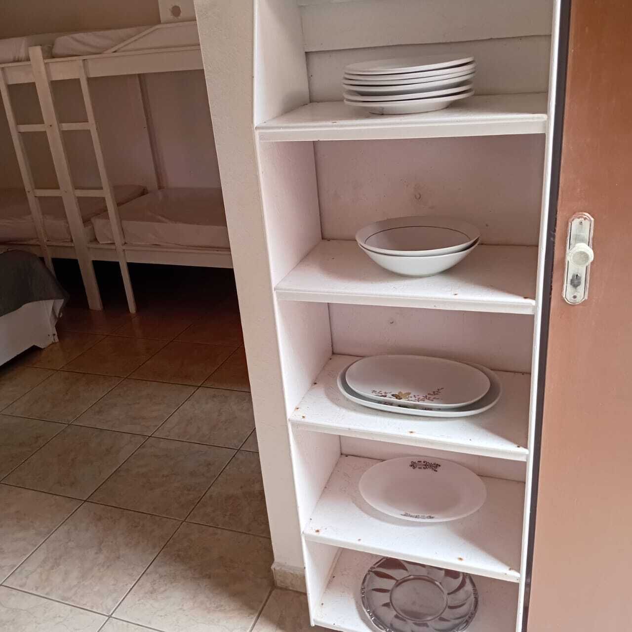 Un lit superposé avec une échelle, une étagère blanche avec des assiettes et une porte avec une poignée.