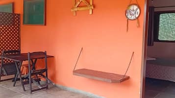Quarto com parede laranja, balanço de madeira, mesa pequena com cadeiras e uma cama ao fundo.