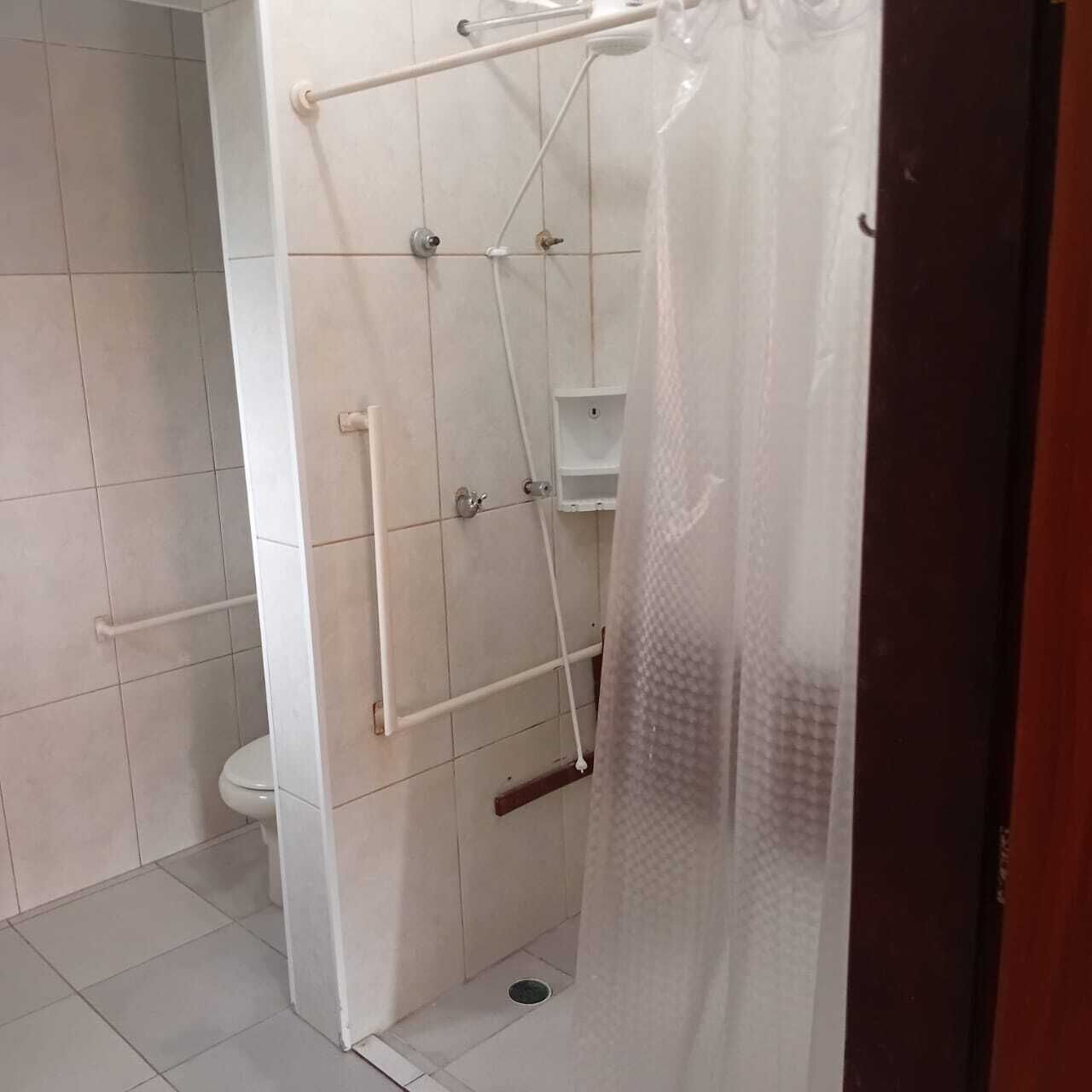 Pequeño espacio cerrado con ducha, inodoro, barra de apoyo y panel de control de la ducha.