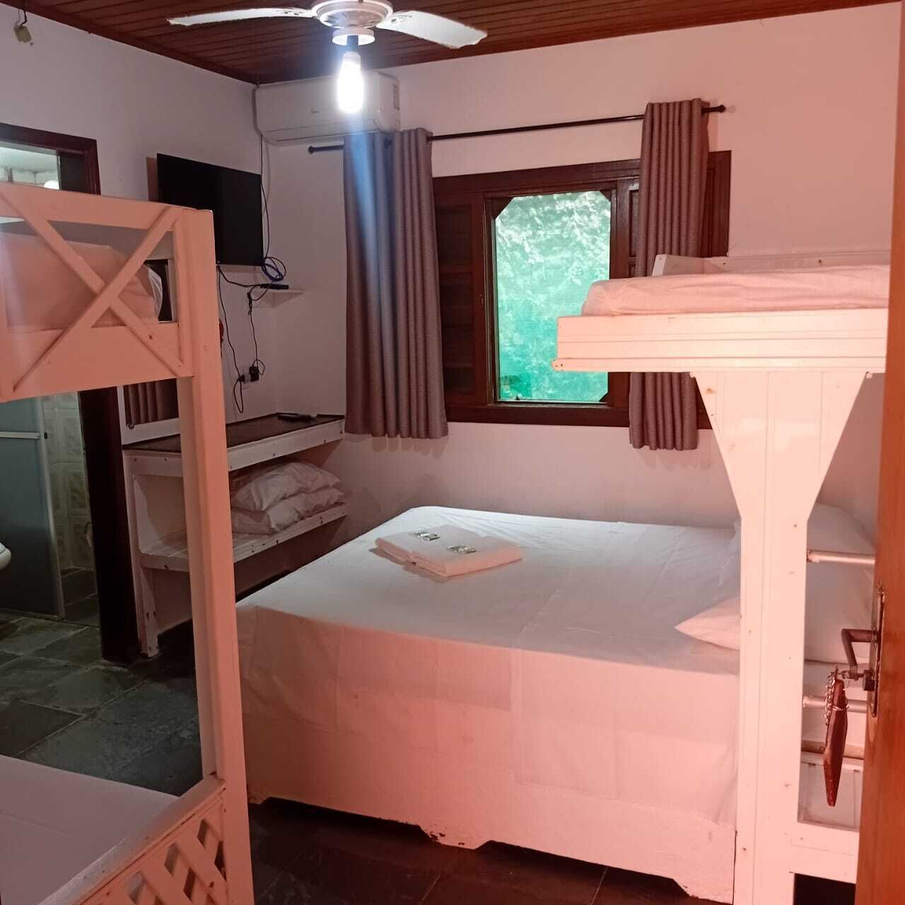 Una habitación con literas, ventilador de techo, ventana con cortinas y televisión.