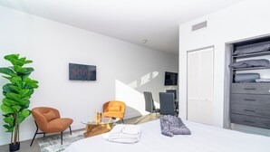 Een moderne slaapkamer met een groot bed, een zithoek met een stoel, een potplant en een garderobe.