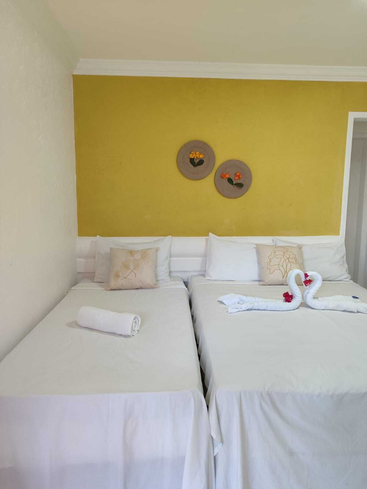 A hotel room with two single beds, white bedding, and a yellow accent wall.