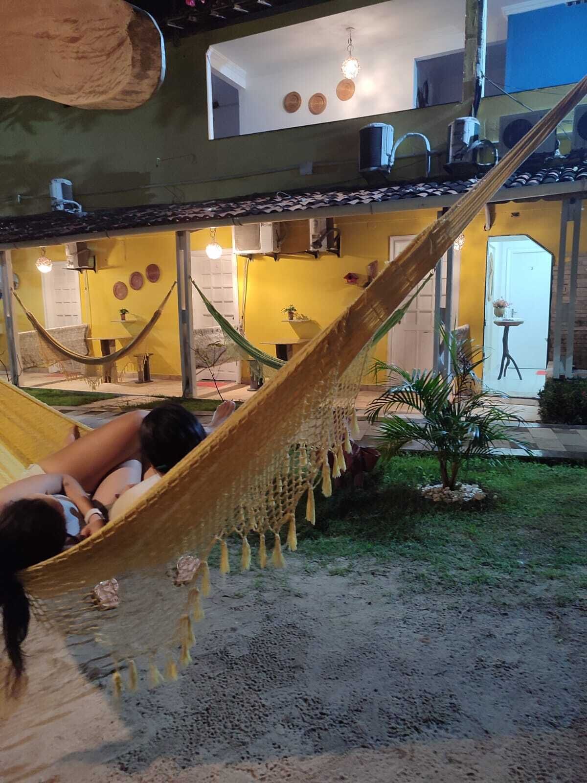 Una hamaca en un patio con un muro amarillo, una palmera pequeña y una puerta al fondo.