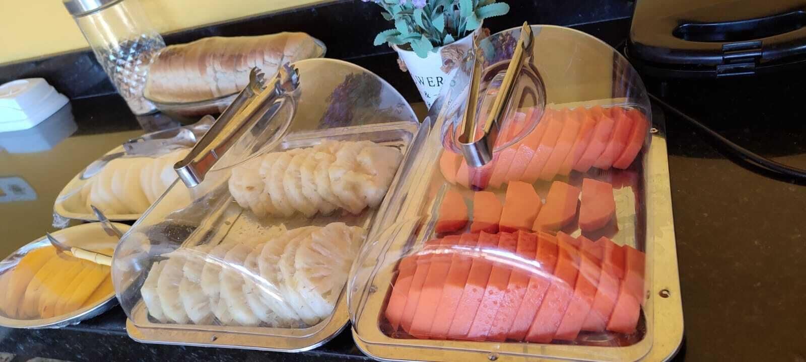 Ein Buffet mit verschiedenen Speisen, darunter Obstscheiben und Gebäck in durchsichtigen Behältern.