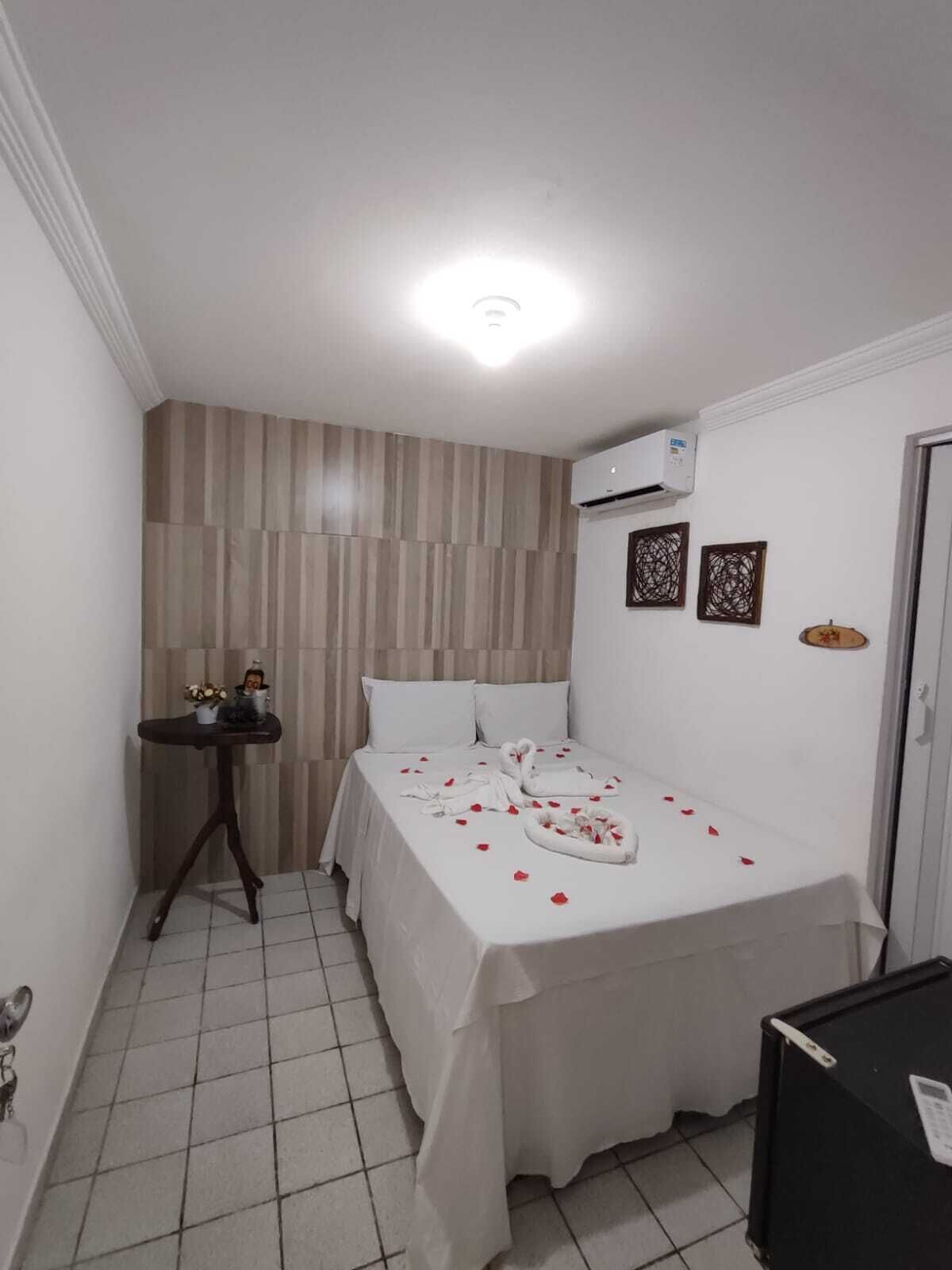Una habitación pequeña y limpia con una cama, una mesita y un equipo de aire acondicionado.