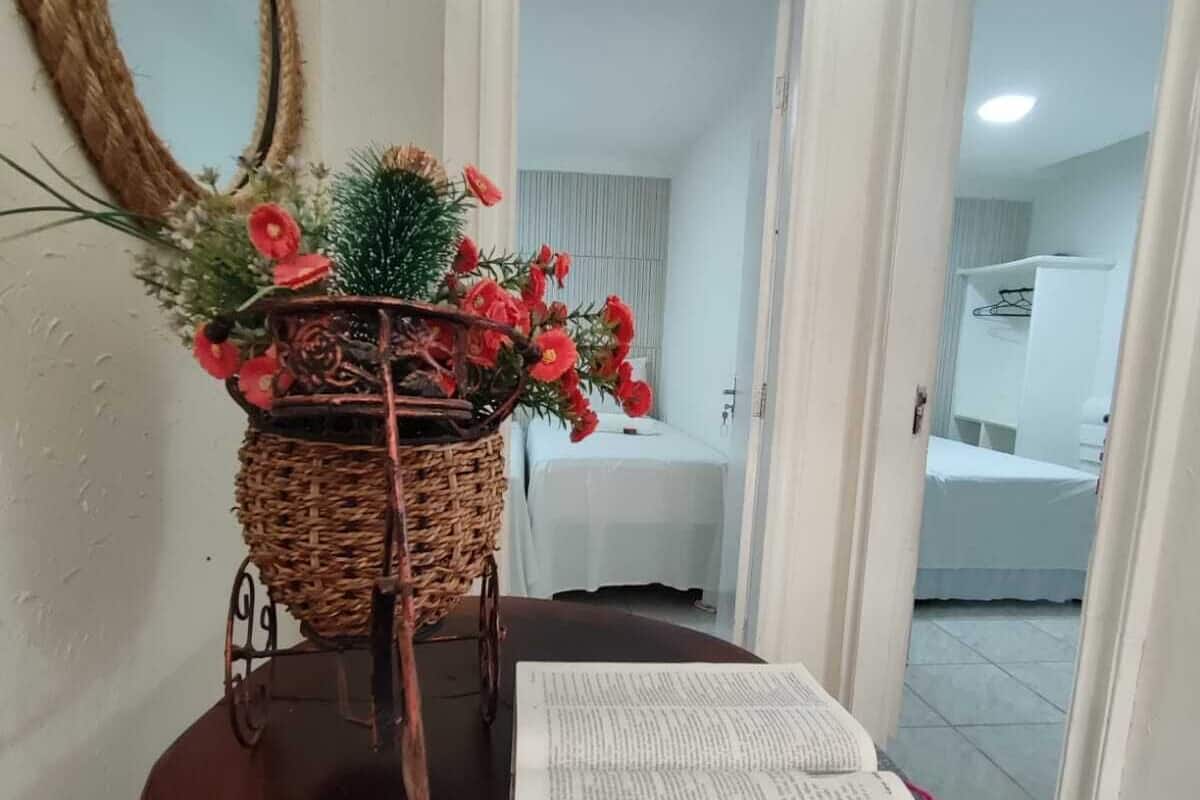 A wooden table with a wicker basket holding red flowers and a potted plant, a mirror on the wall, and a doorway leading to a bathroom.