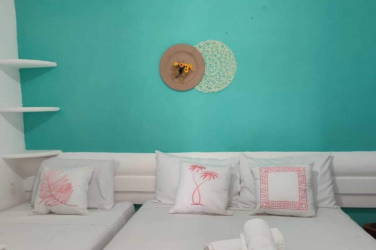 A room with a teal wall, white furniture, and decorative pillows with floral and geometric designs.