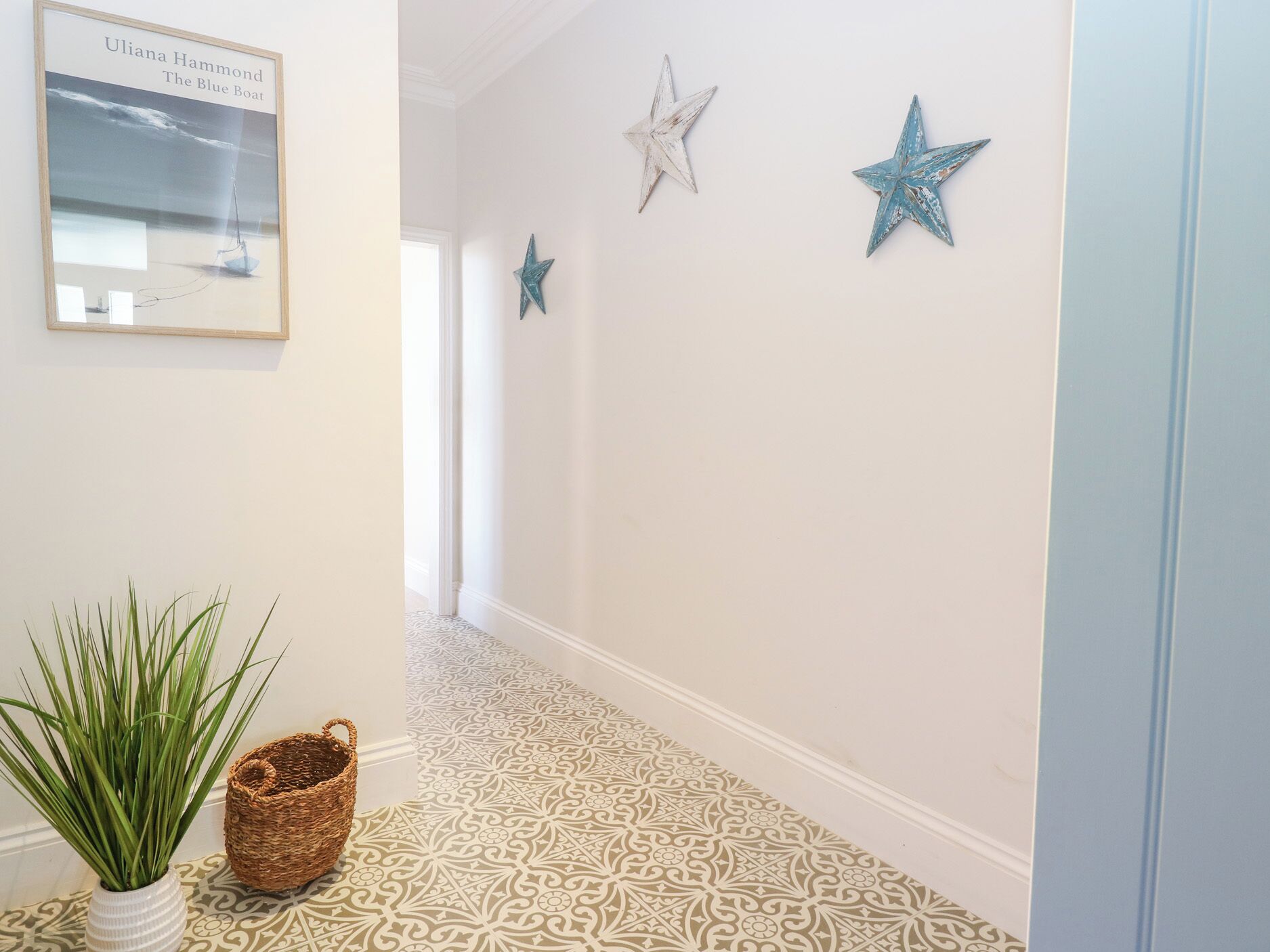 A hallway with patterned floor tiles, a framed picture of a boat, and three star decorations on the wall.