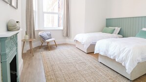 Ein Schlafzimmer mit zwei Betten, einem kleinen Stuhl, einem Kamin und einem Fenster mit Vorhängen.