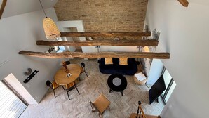 A loft-style room with a stone wall, wooden beams, a dining area with a round table, and hanging woven light fixtures.