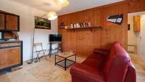 A living room with a red leather sofa, a coffee table, a TV, a bookshelf, and wooden paneling on the walls.